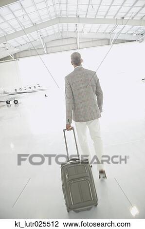 Stock Image - Man with suitcase walking out of airplane hanger, Nobato, California, United States. Fotosearch