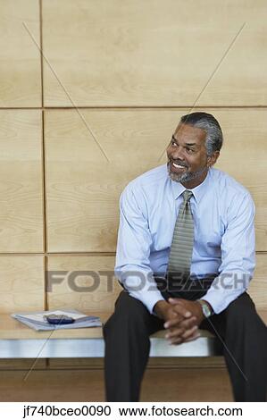 Middle-aged African businessman sitting on bench indoors View Large Photo Image Stock Image - Middle-aged African businessman sitting on bench indoors. Fotosearch