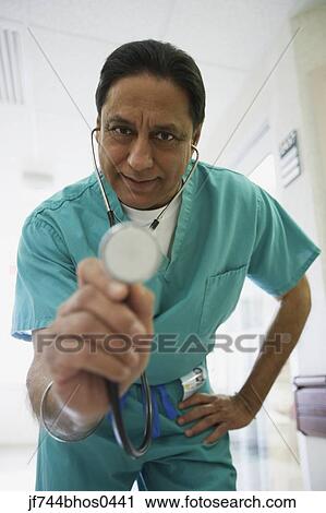Stock Image - Middle-aged Indian male doctor holding out stethoscope, Bethesda, Maryland, United States. Fotosearch