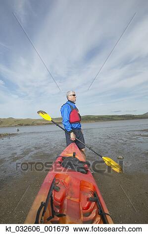 Stock Photo - Middle-aged man holding kayak and paddle, California, United States. Fotosearch