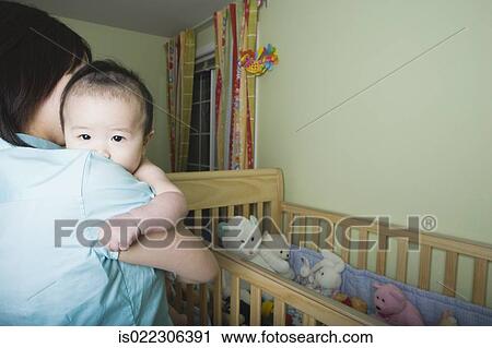 Mother holding Asian baby next to crib View Large Photo Image Stock Image - Mother holding Asian baby next to crib. Fotosearch