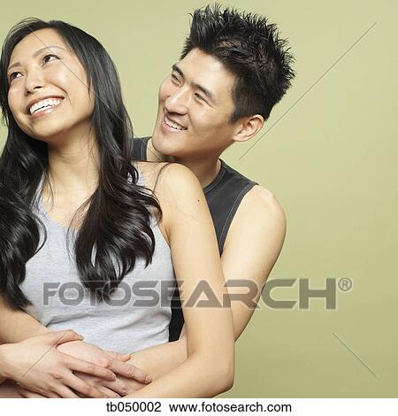 Stock Image - Studio shot of young Asian couple hugging. Fotosearch