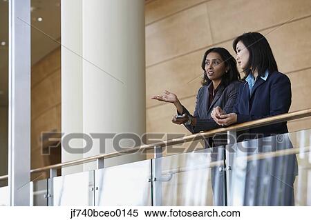 Two businesswomen talking at railing View Large Photo Image Stock Photography - Two businesswomen talking at railing. Fotosearch