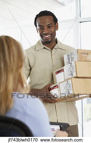 Stock Image - Woman signing for packages from African deliveryman. Fotosearch