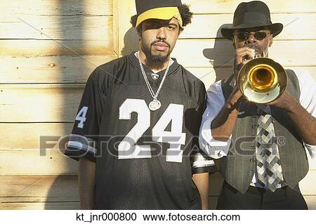 Stock Image - Young African man standing next to senior African man playing trumpet, Oakland, California, United States. Fotosearch