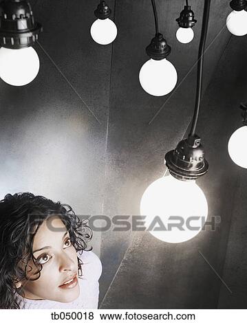 Stock Photo - Young woman looking up at a light bulb. Fotosearch
