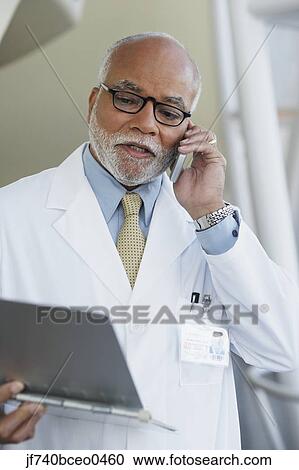 Stock Bild - älterer mann, afrikanisch, doktor, unterhaltung zelle telefon, mit, tabelle. Fotosearch