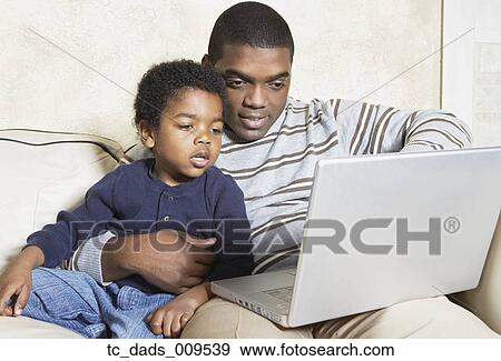 Stock Photo - African American father and young son with laptop on sofa. Fotosearch