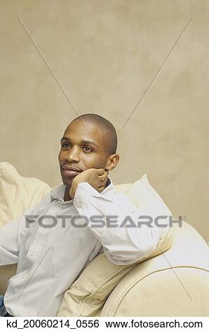 Stock Photograph - African American man sitting on sofa. Fotosearch