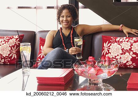 Stock Photograph - African American woman sitting on sofa with drink. Fotosearch