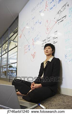 Stock Image - Asian businesswoman with laptop on floor in front of whiteboard wall. Fotosearch
