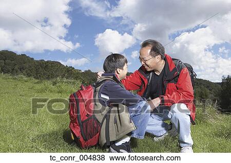 Stock Photo - Asian father and son with backpacks outdoors. Fotosearch