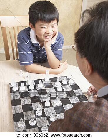 Stock Image - Asian father and young son playing chess . Fotosearch