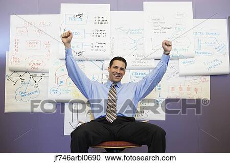 Stock Image - Businessman cheering in front of wall charts. Fotosearch
