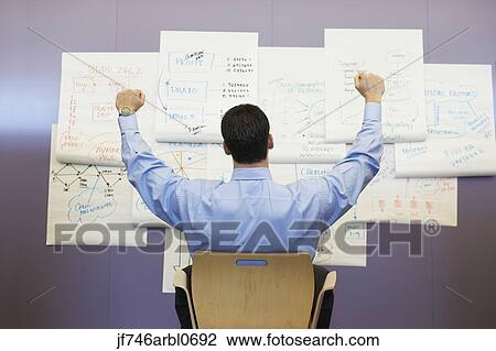 Stock Image - Businessman cheering in front of wall charts. Fotosearch