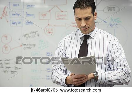 Stock Photography - Businessman reading paperwork in front of whiteboard. Fotosearch