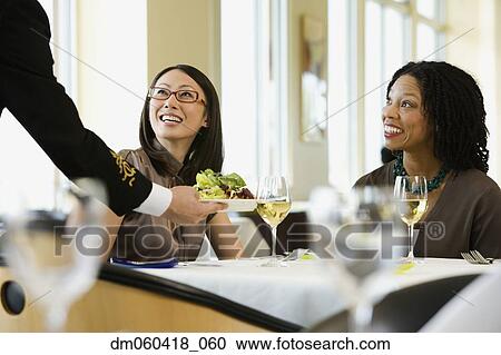 Stock Image - Businesswomen being served in restaurant. Fotosearch