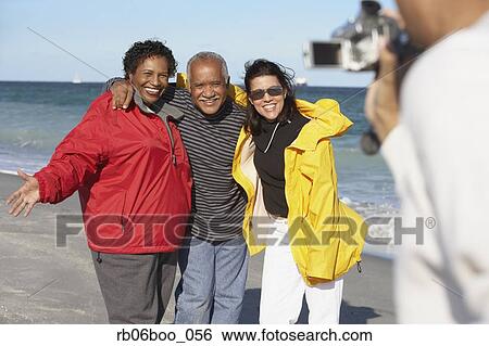 Stock Photograph - Group of middle-aged friends using video camera at beach. Fotosearch