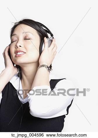 Stock Photograph - Studio shot of Asian woman listening to music with headphones. Fotosearch