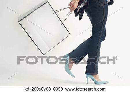 Stock Image - Studio shot of woman walking with shopping bag. Fotosearch