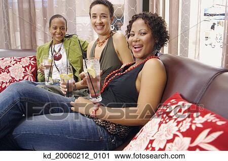 Stock Image - Three women smiling and drinking on sofa. Fotosearch