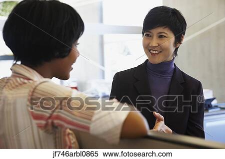 Two female coworkers talking in office View Large Photo Image Stock Photography - Two female coworkers talking in office. Fotosearch