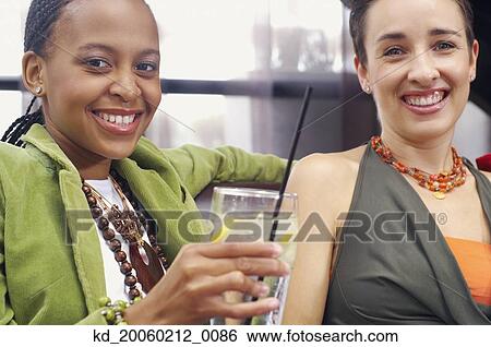 Stock Photograph - Two women sitting on sofa smiling. Fotosearch