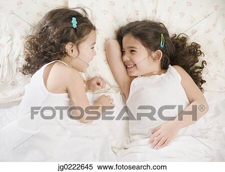 Stock Photography - Two young Hispanic sisters giggling in bed. Fotosearch