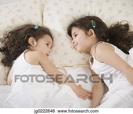 Stock Photograph - Two young Hispanic sisters lying in bed. Fotosearch