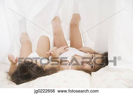 Stock Photograph - Two young Hispanic sisters playing under sheet. Fotosearch