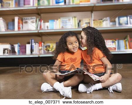 Stock Image - Two young sisters whispering in library. Fotosearch