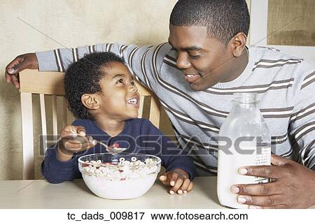 Stock Photo - Young African American boy eating cereal with father. Fotosearch