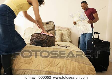 Stock Image - African couple packing suitcase on bed. Fotosearch