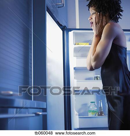 Stock Photo - African woman looking in refrigerator with excitement. Fotosearch