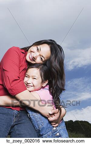 Stock Photograph - Asian mother and daughter hugging outdoors. Fotosearch