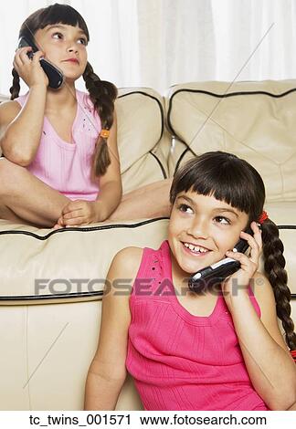 Stock Image - Hispanic sisters using cell phones on sofa. Fotosearch