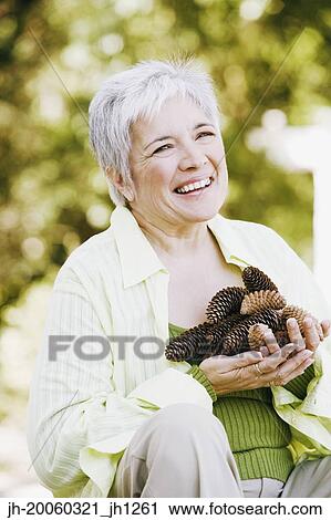Stock Image - Middle-aged woman holding handful of pinecones outdoors. Fotosearch