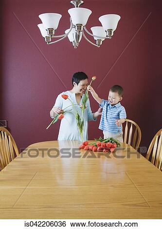 Stock Photograph - Mother and young son putting flowers in vase. Fotosearch