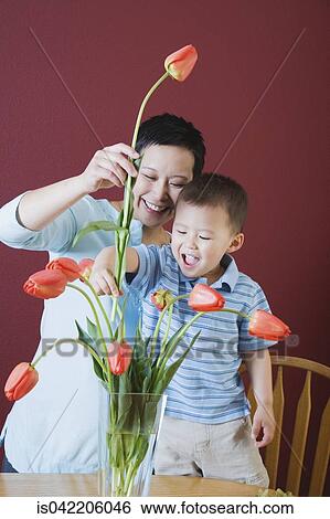 Stock Photograph - Mother and young son putting flowers in vase. Fotosearch