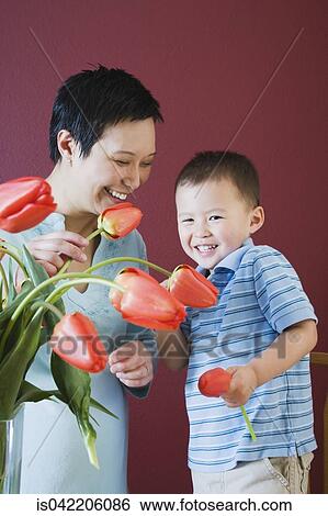 Stock Photograph - Mother and young son putting flowers in vase. Fotosearch