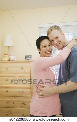 Stock Image - Pregnant couple hugging indoors . Fotosearch