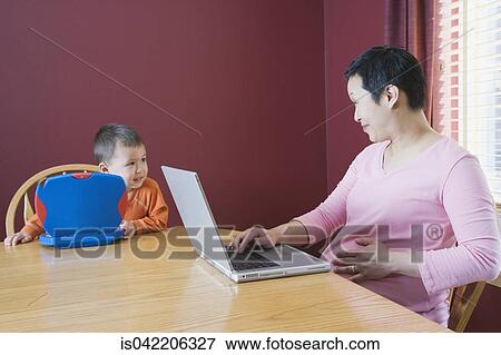 Stock Photo - Pregnant woman working at home with young son. Fotosearch
