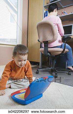 Stock Photo - Woman working at home with young son. Fotosearch