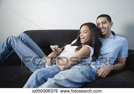 Young African couple watching television on sofa View Large Photo Image Stock Photo - Young African couple watching television on sofa. Fotosearch