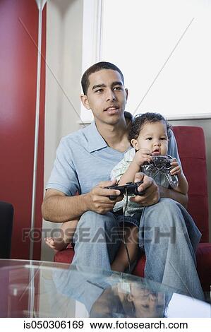 Stock Photo - Young African father playing video games with baby on lap. Fotosearch