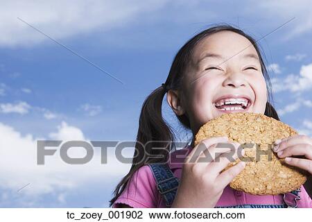 Stock Image - Young Asian girl holding cookie outdoors. Fotosearch