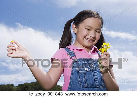 Stock Image - Young Asian girl holding flowers outdoors. Fotosearch