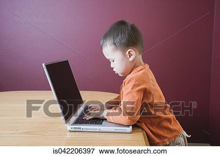 Stock Photo - Young boy using laptop at table. Fotosearch