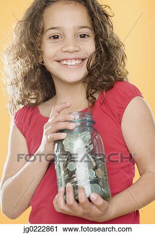 Stock Image - Young girl holding jar full of money. Fotosearch
