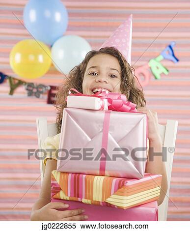 Stock Photography - Young girl holding stack of gifts at birthday party. Fotosearch